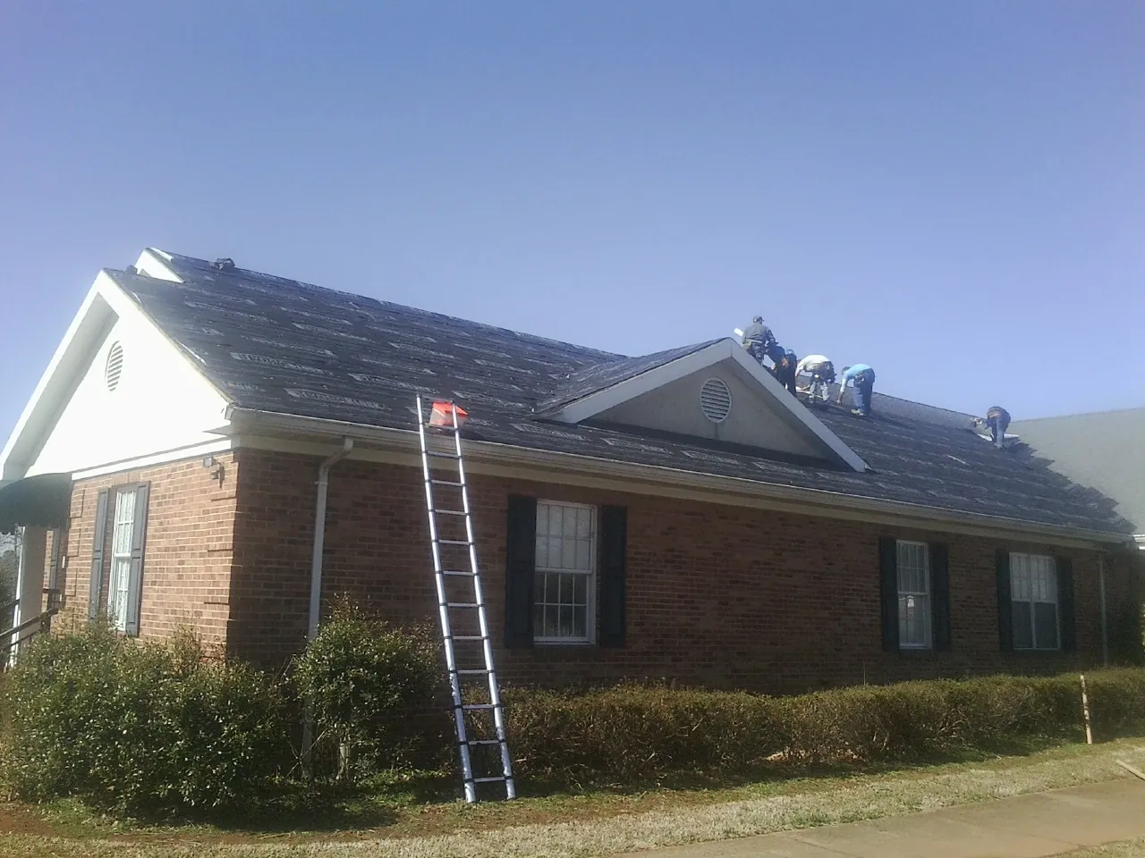 Crew tearing shingles off a brick ranch roof with a ladder set — Metal Roof Repair work by our crew in West Milton