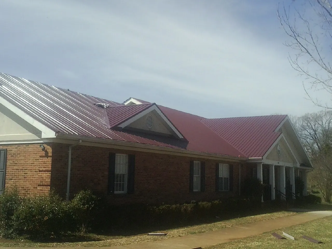 Red metal roof with gabled entries on a long brick building, from a Hail Damage Roof Repair job in West Milton