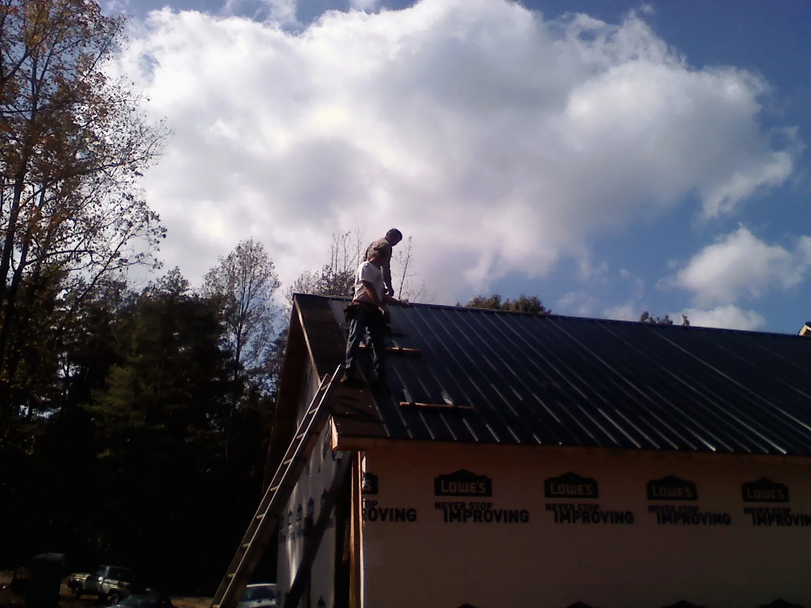 Roofer fastening dark metal panels high against a cloudy sky, from a Roof Inspection job in West Milton
