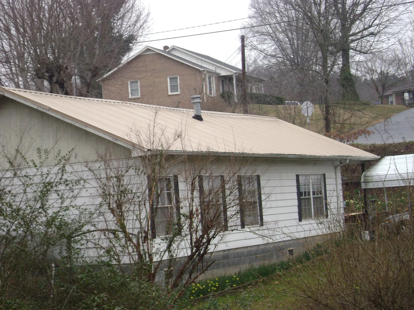Tan metal roof on a white sided house set into a hillside — Commercial Roofing by Roofing Brothers in West Milton